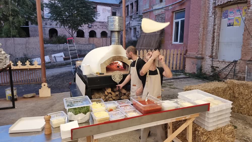 A pizza base thrown into the air beside the mobile oven