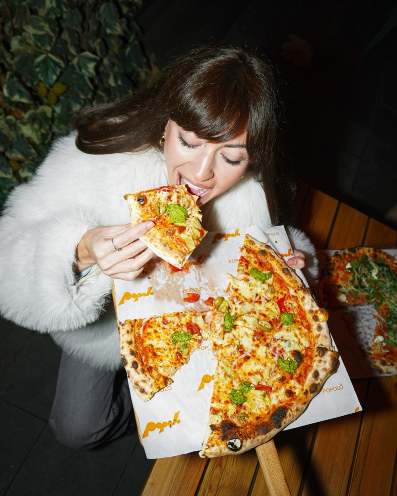 A guest biting into a slice over a freshly baked pizza