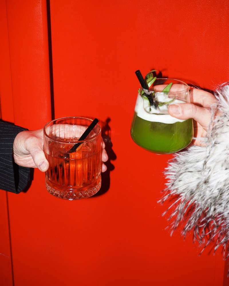 Two cocktails raised against the red wall
