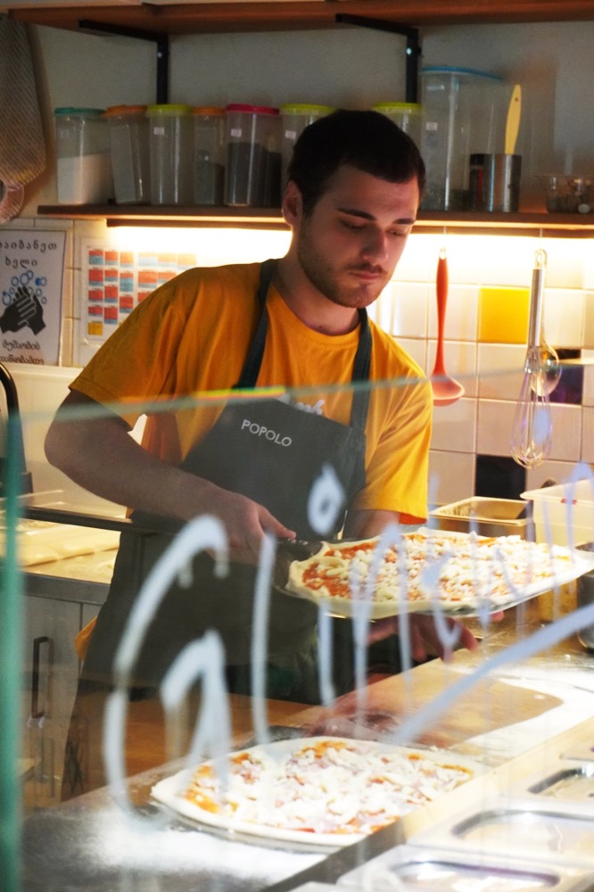 A cook in a Popolo apron building a pizza behind the counter