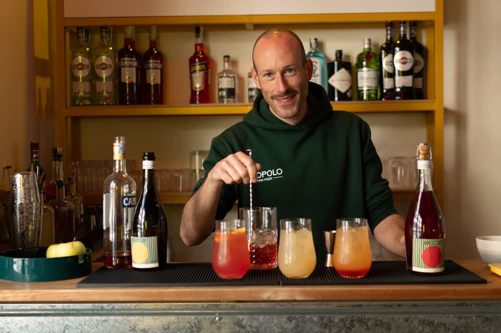 A bartender in a Popolo hoodie mixing drinks at the bar